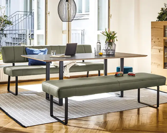 Moderne Essgruppe mit Esstisch, gepolsterter Sitzbank und Eckbank in Grün, kombiniert mit Metallgestell und Teppich, heller Essbereich mit großen Fenstern und wohnlicher Atmosphäre